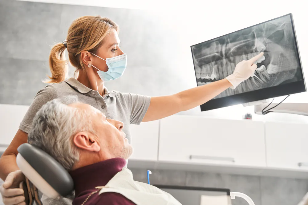 A close up image of a dentist placing an oral implant into a patient's mouth, with dental tools visible. No text on image.