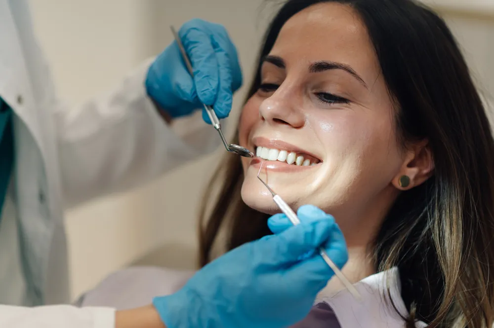 A periodontist examining a patient's mouth, focusing on the gums, using specialized dental instruments. No text on image.
